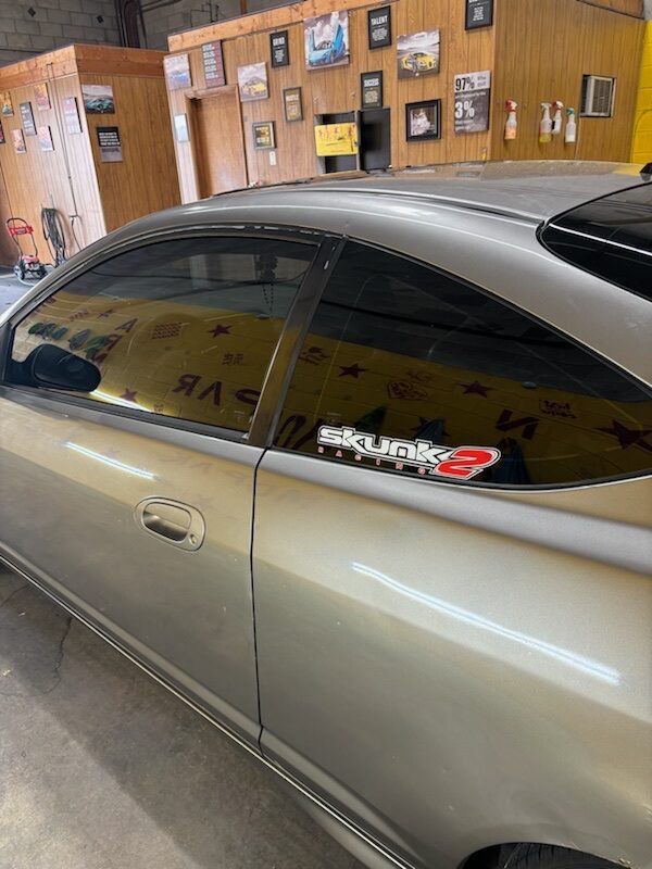 Custom gold-tinted coupe in the shop, parked in front of the wall of achievement plaques